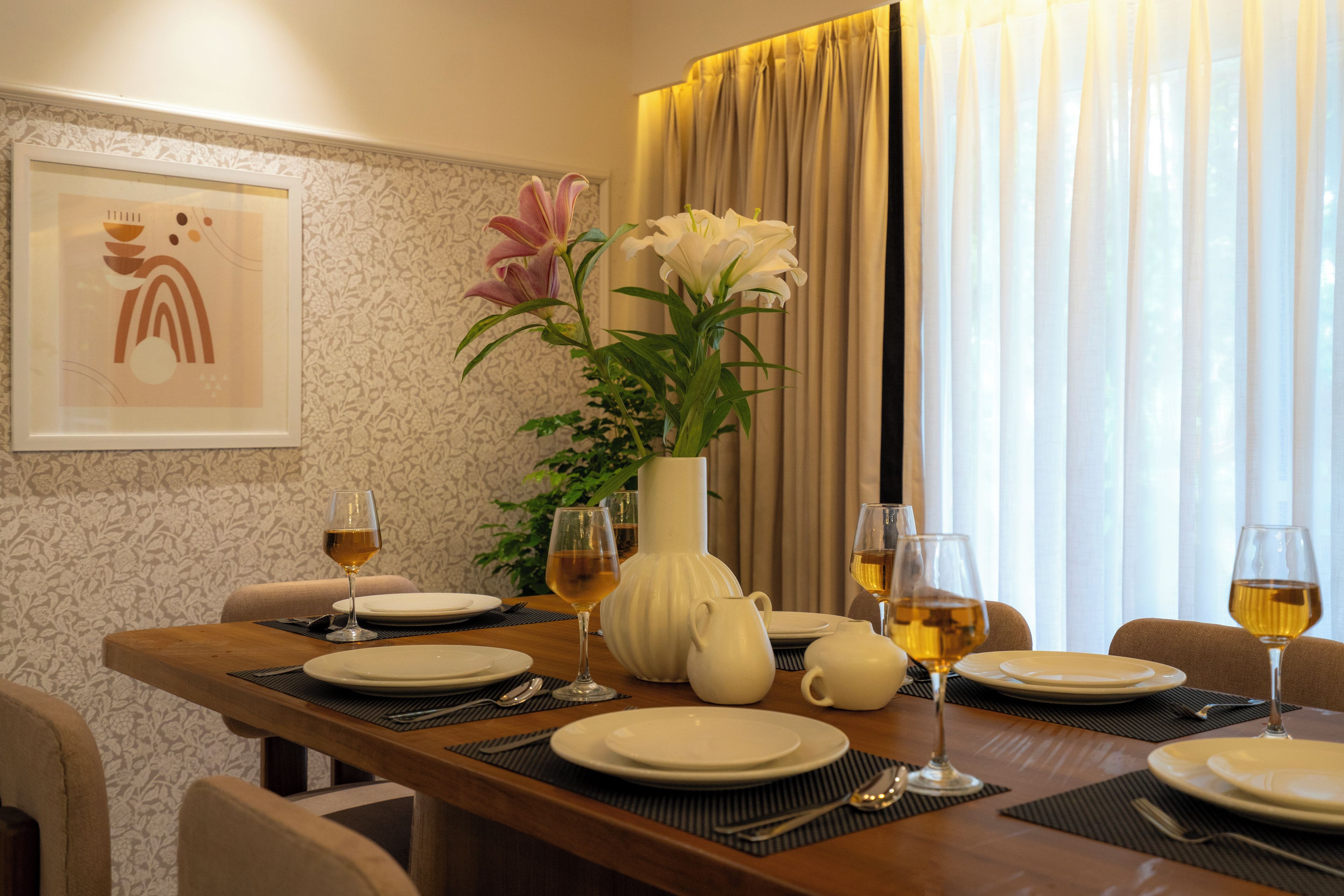 A dining table set for four with white plates, wine glasses, and a vase with flowers.
