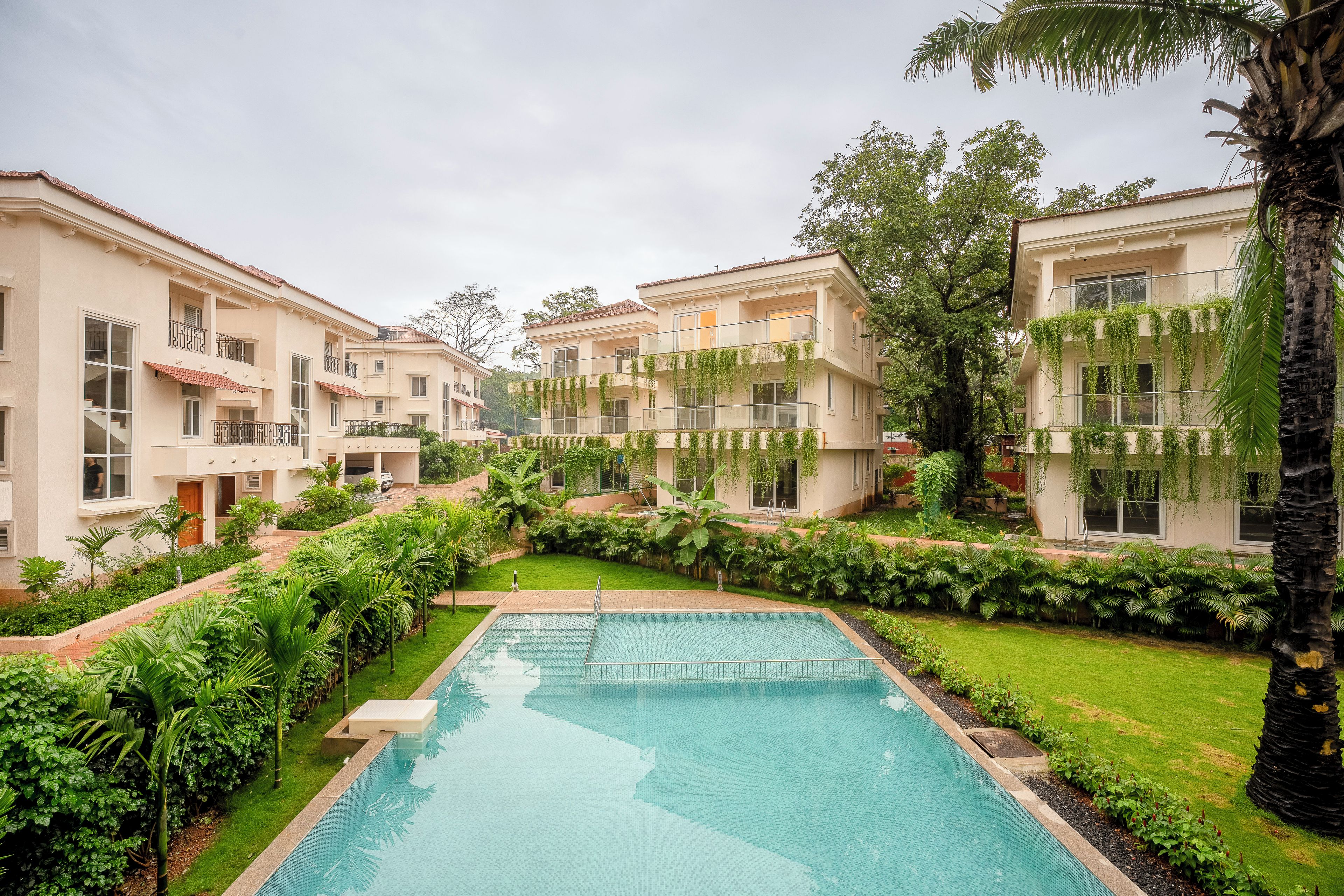 Um edifício residencial com piscina, rodeado por vegetação exuberante e palmeiras.
