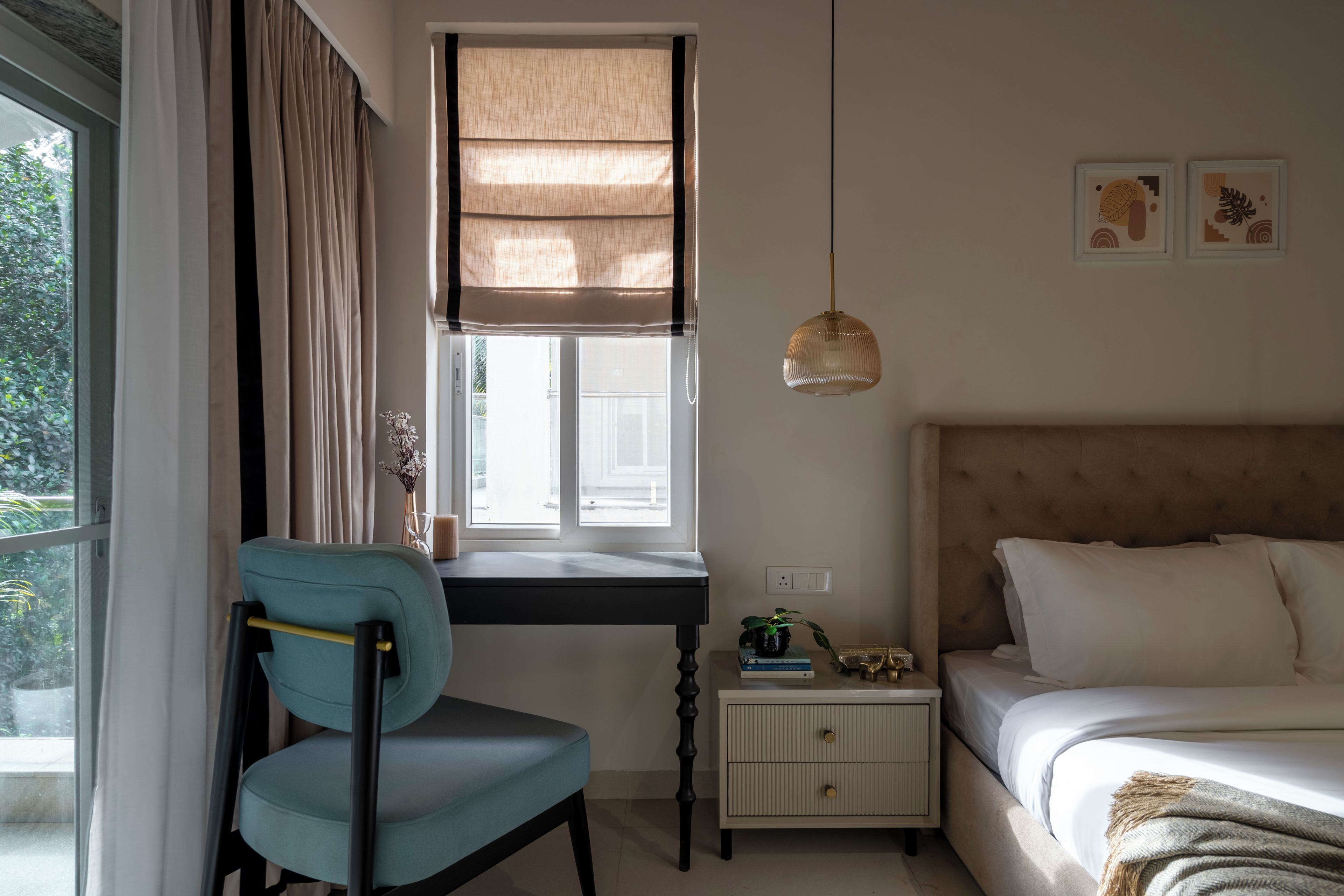 A bedroom with a bed, a desk with a chair, a bedside table with a lamp, and a window with curtains.