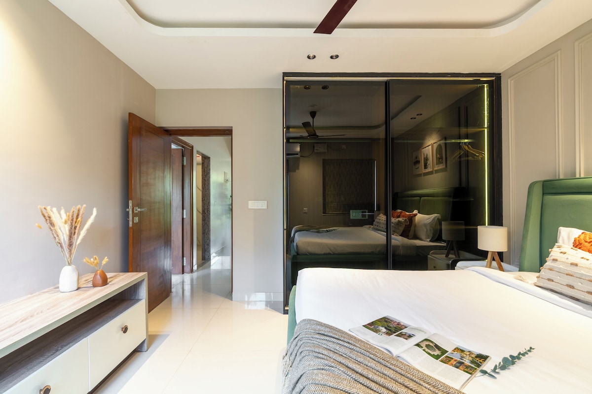Quarto moderno com cama grande, mesa de cabeceira, espelho e guarda-roupa.