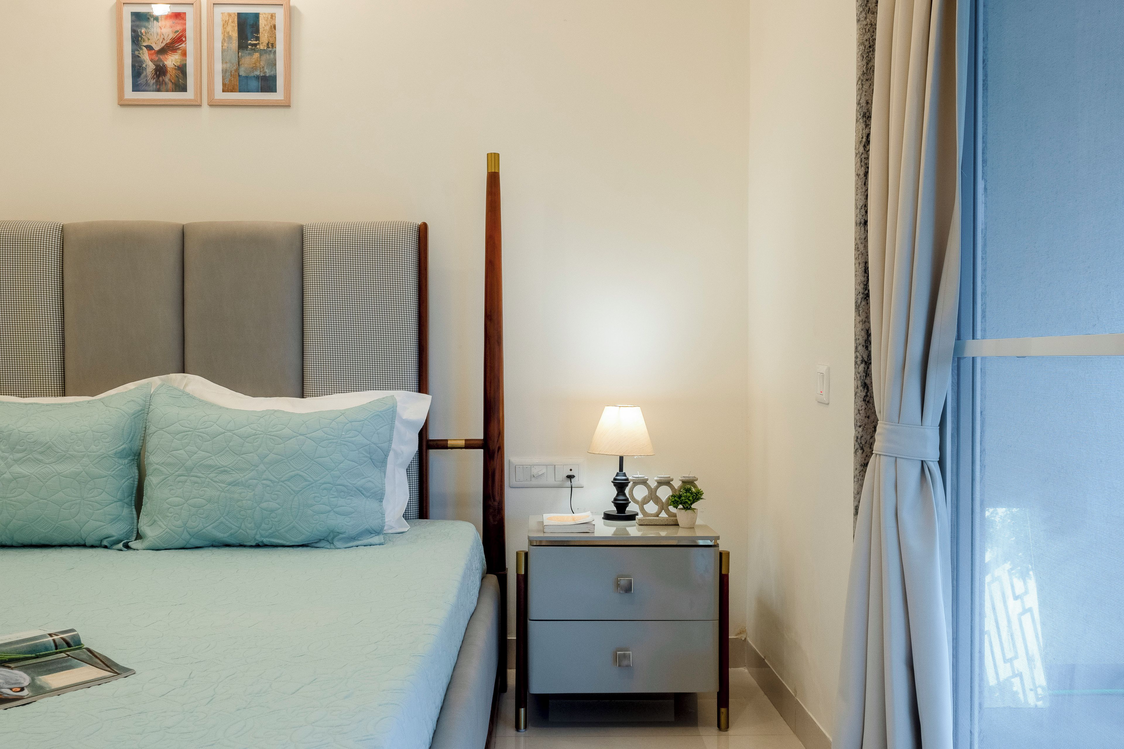 Habitación de hotel ordenada con cama, mesita de noche, lámpara y ventana con cortinas.