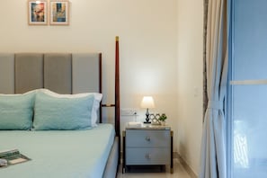 A neatly arranged hotel room with a bed, bedside table, lamp, and a window with curtains. - Staymaster Terra-4BR Villas w Pool & Gym (Siolim)