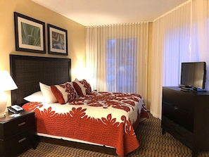 Ein Hotelzimmer mit einem Bett, einem Nachttisch, einem Fernseher auf einer Kommode und zwei gerahmten Bildern an der Wand.