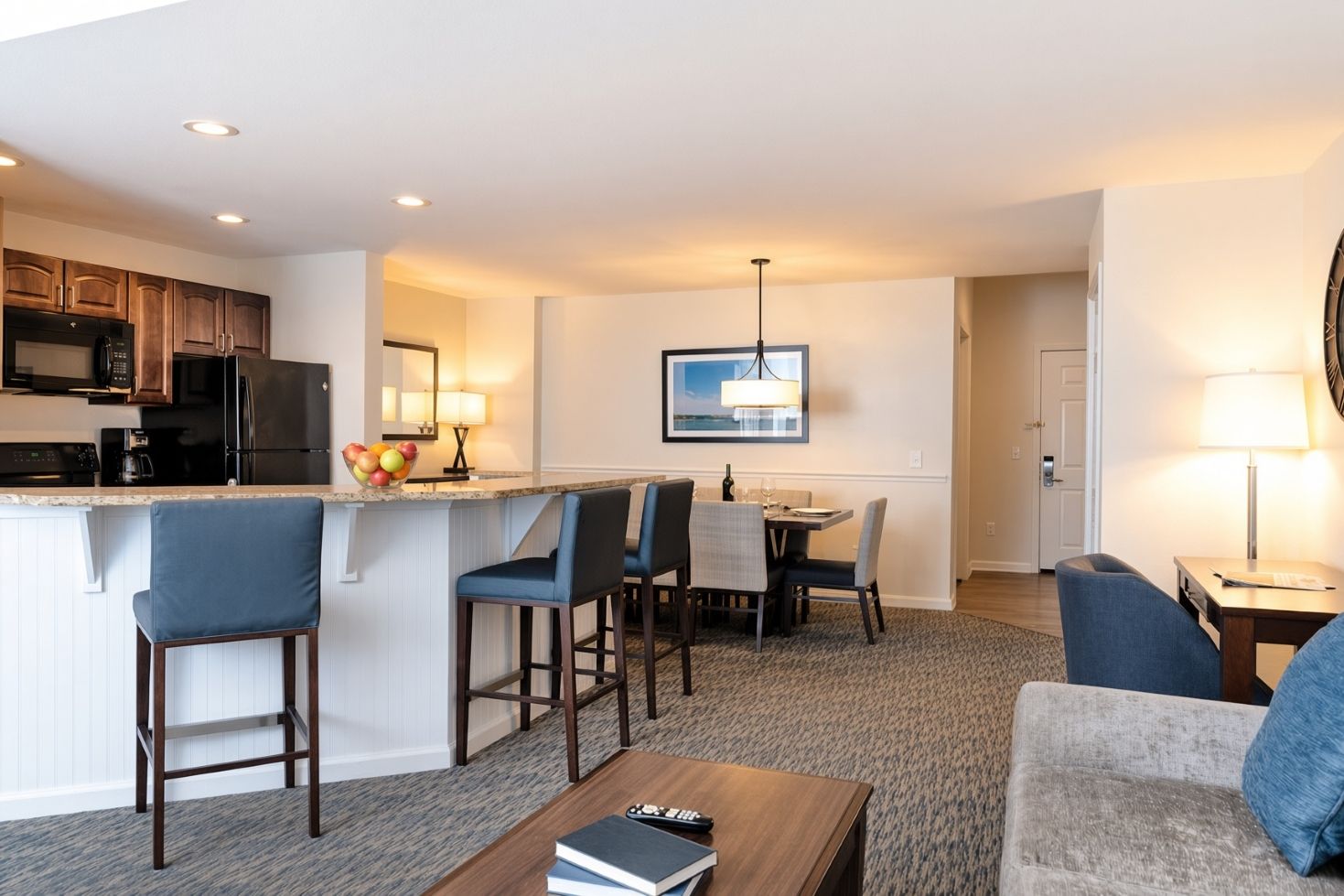 A modern hotel room with a kitchenette, a dining area, and a living space.