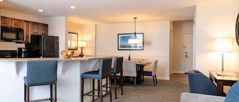 A modern hotel room with a kitchenette, a dining area, and a living space.