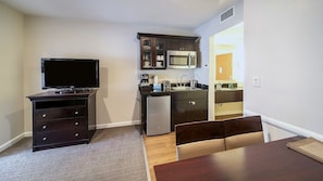 A compact living space with a TV, dark wooden furniture, a kitchenette, and a dining area. - Anaheim | Couples Magic Getaway | Pool + Hot Tub (Anaheim)