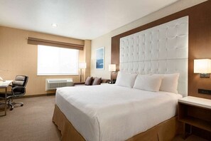 Una camera d'albergo con un letto grande, una scrivania con sedia, una finestra e una lampada fissata al muro.