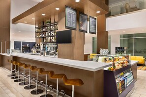 Zona bar moderna con un lungo bancone, diversi sgabelli e una vetrina con prodotti alimentari.