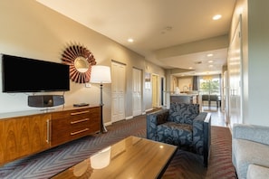 A hotel room with a flat-screen TV, a wooden cabinet, a patterned sofa, and a dining area in the background. - Indio CA | Desert Relaxation Trip | Pool & Lazy River | 2BR (Indio)