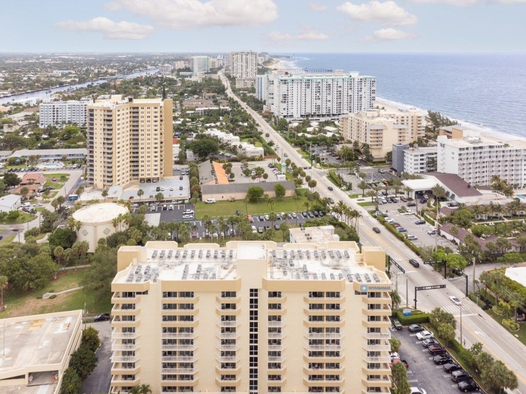 A high-rise hotel with multiple floors, a parking lot, and a view of the ocean.