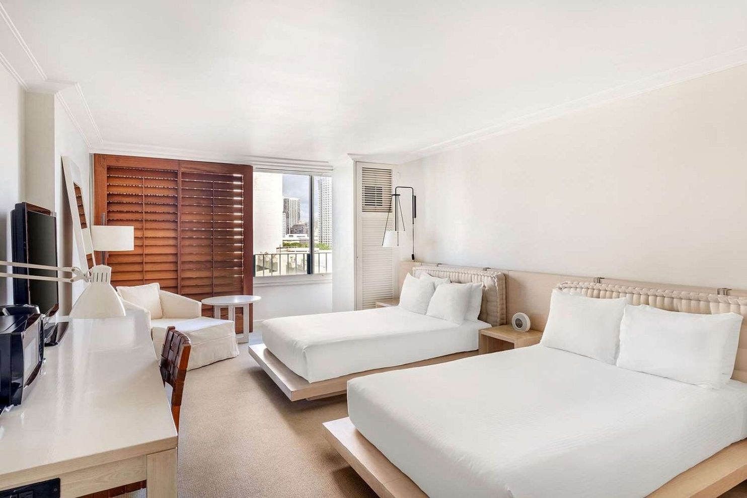 Une chambre d’hôtel avec deux lits, un bureau, une chaise, une télévision et une fenêtre avec des stores.