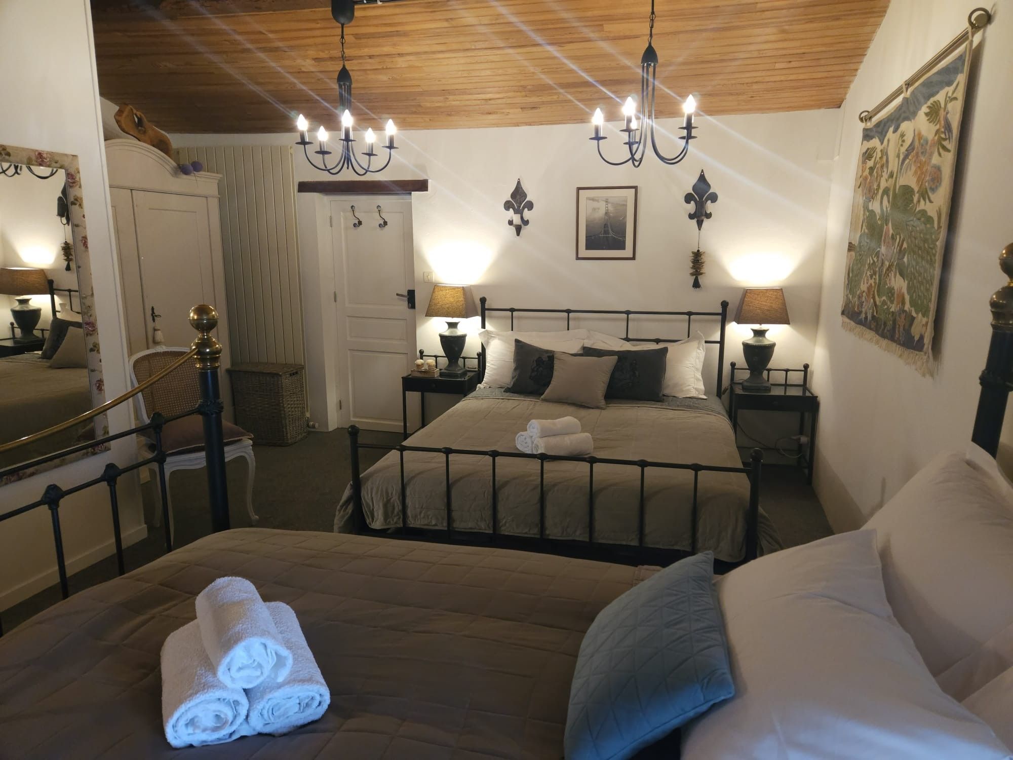 Une chambre à coucher avec un lit, deux tables de chevet avec des lampes, un lustre, une porte et un tableau au mur.