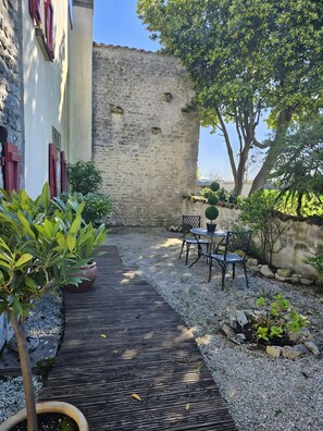 Un patio con un sendero de grava, una mesa con sillas y plantas en macetas.