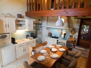 Una cocina con armarios blancos, una mesa de comedor de madera dispuesta para cuatro personas y vistas al exterior a través de una ventana.