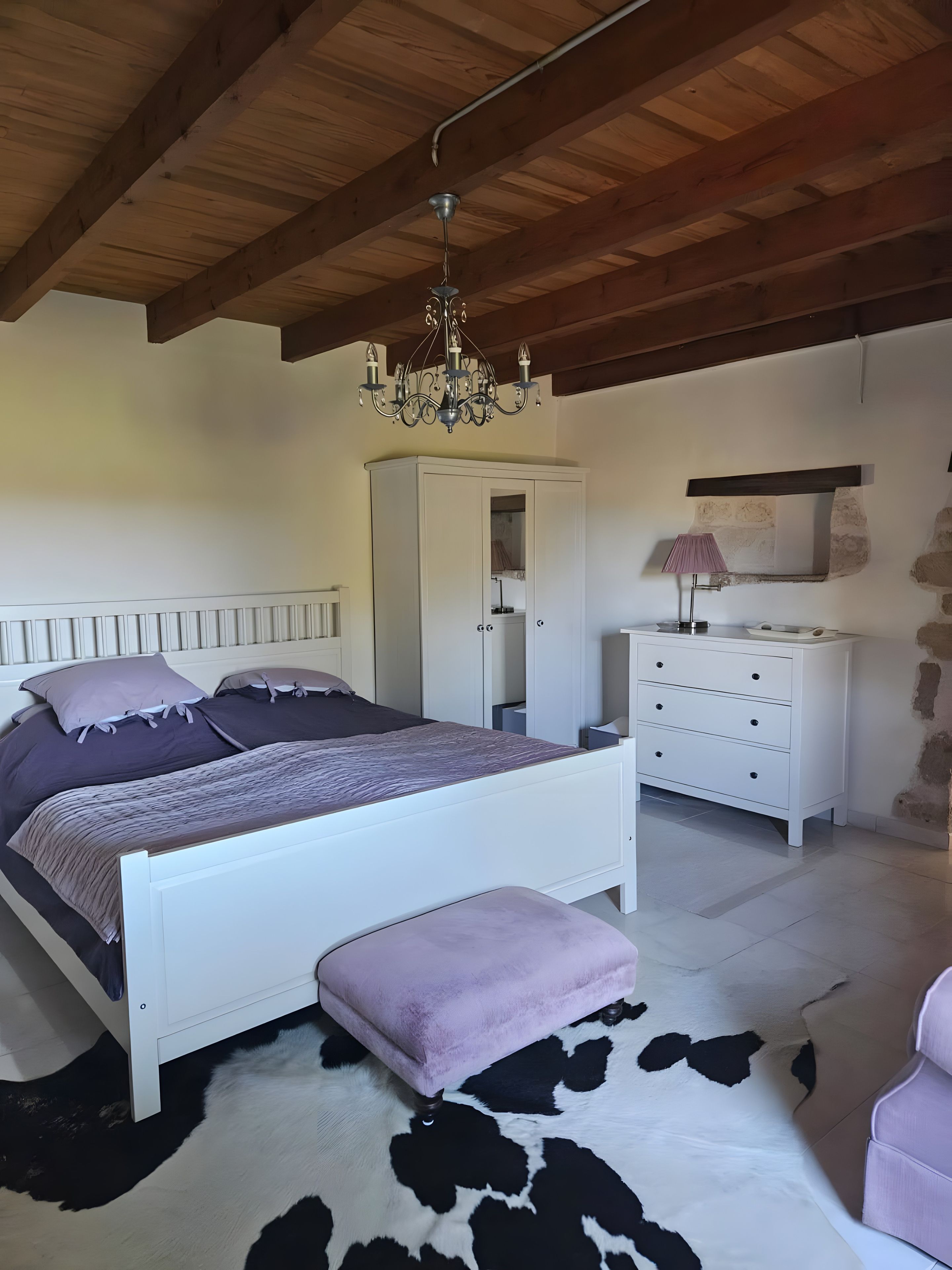 Een slaapkamer met een bed, een kledingkast, een dressoir, een kroonluchter en een stenen muur.