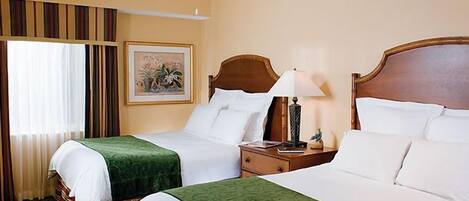 A hotel room with two beds, a ceiling fan, a nightstand with a lamp, and a framed picture on the wall.