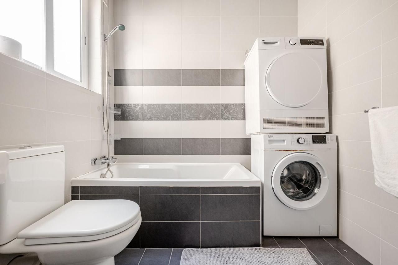 Un baño moderno con inodoro blanco, una bañera y una lavadora de carga frontal.