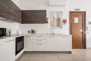A modern kitchen with white cabinetry, a built-in oven, a microwave, and a sink. - JOSEPH COURT F3 (Il-Gżira)