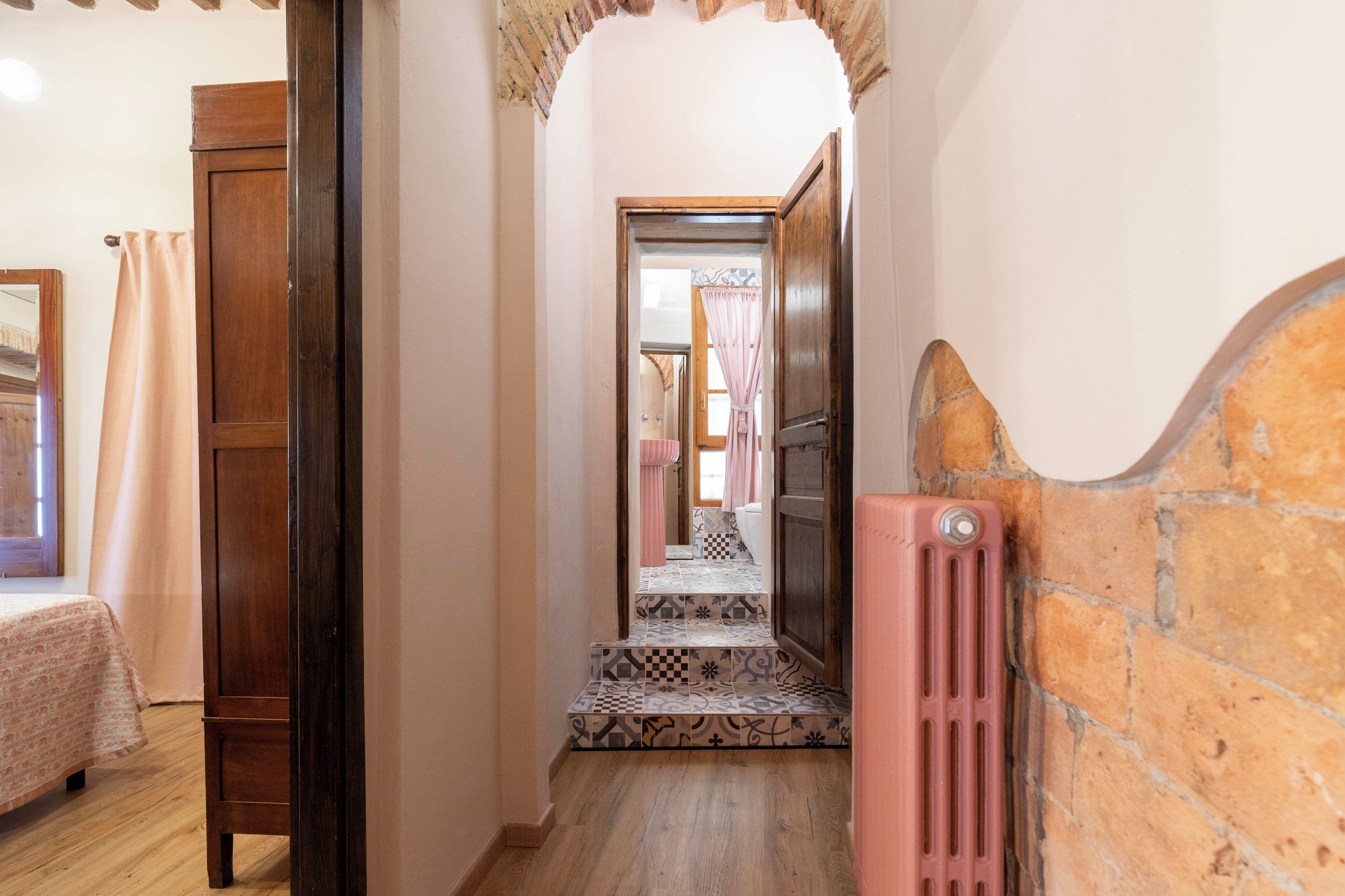 A narrow hallway with wooden doors, a radiator, and patterned floor tiles.