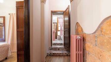 A narrow hallway with wooden doors, a radiator, and patterned floor tiles.