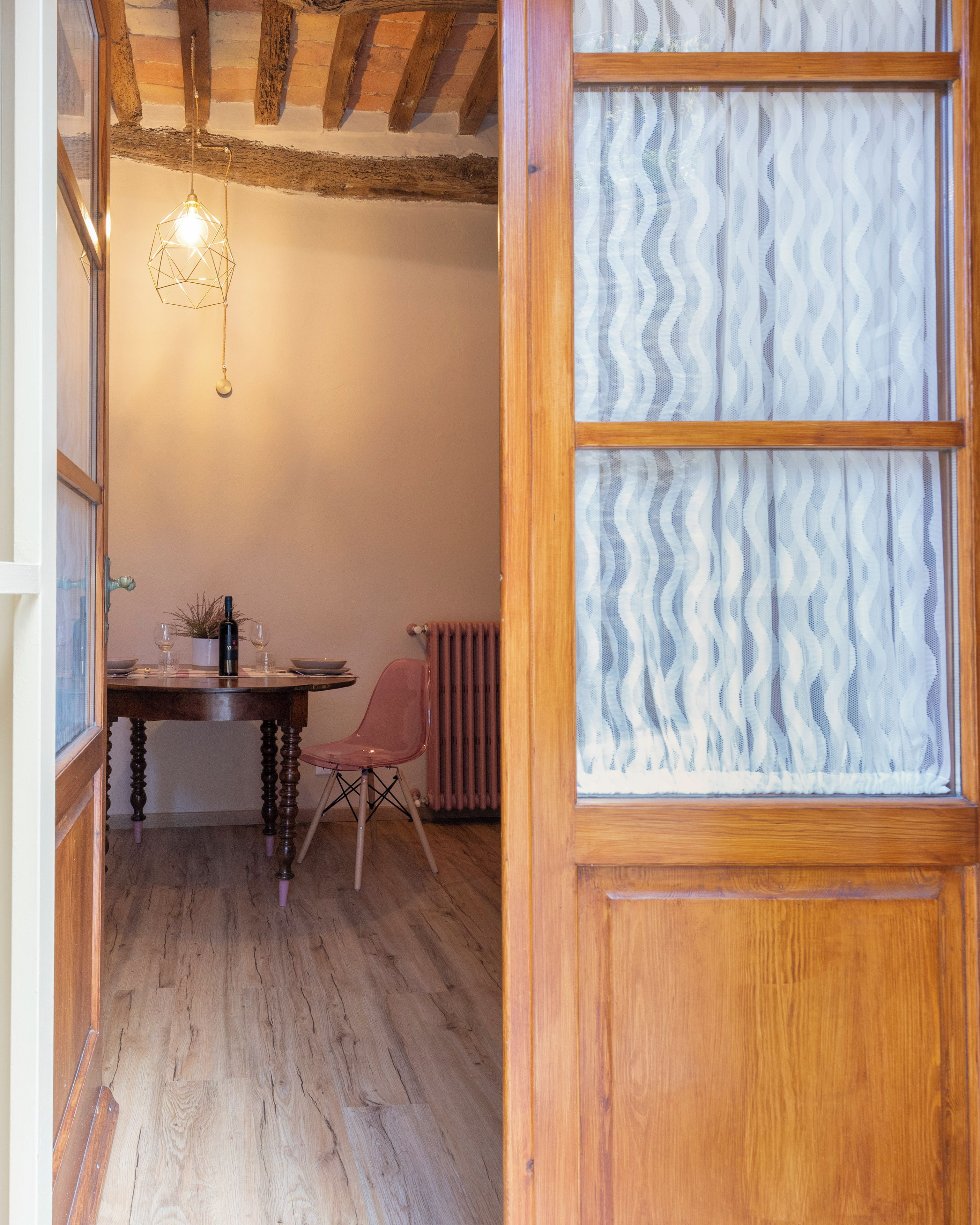 A room with a wooden table, a chair, a hanging light fixture, and a window with a patterned blind.