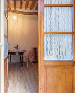 Ein Zimmer mit einem Holztisch, einem Stuhl, einer Pendelleuchte und einem Fenster mit einem gemusterten Jalousie.
