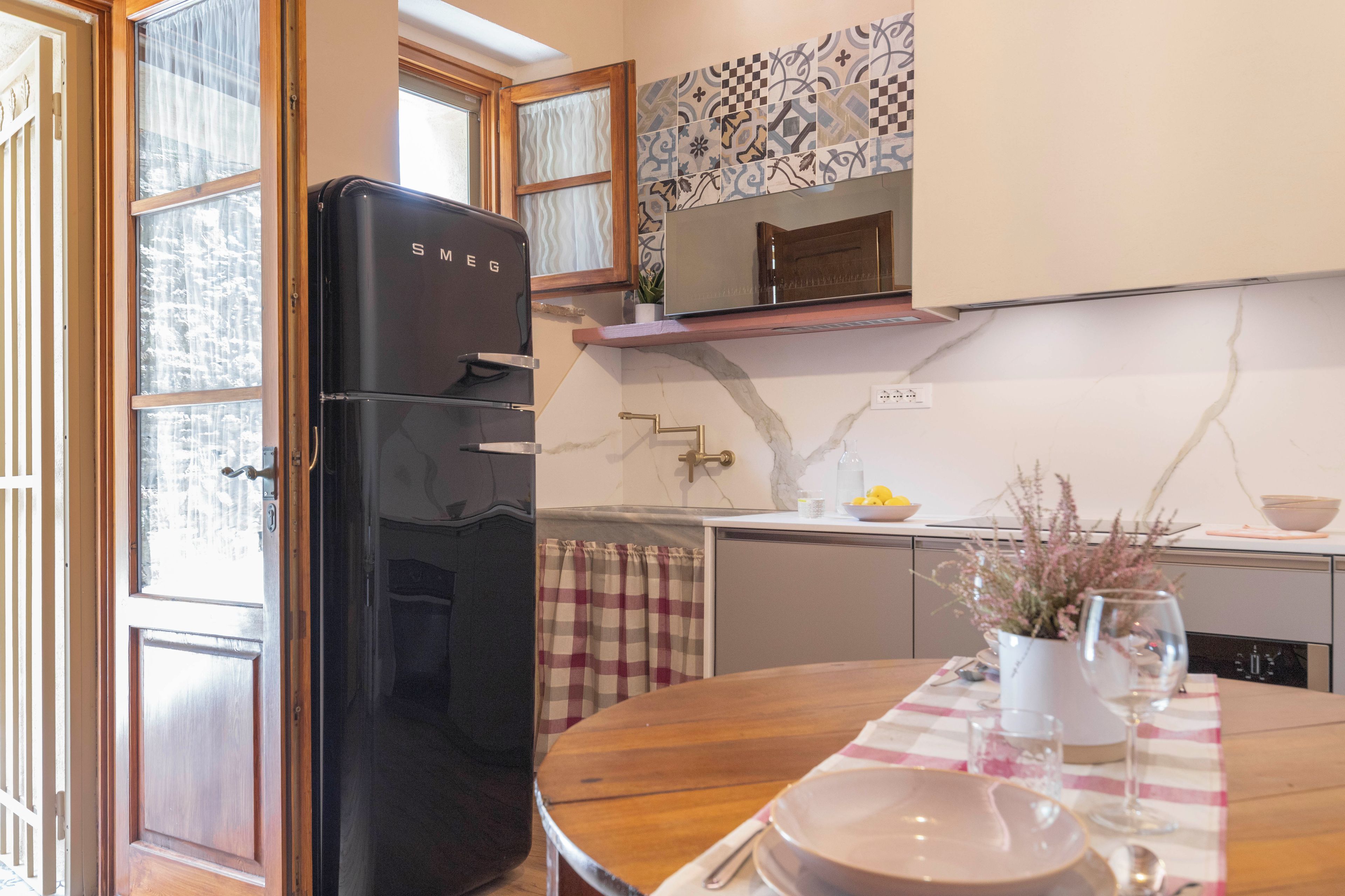 A kitchen with a black refrigerator, a marble backsplash, and a dining table set with plates and glasses.