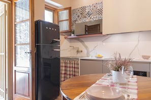 Una cocina con un refrigerador negro, una salpicadura de mármol y una mesa de comedor dispuesta con platos y vasos.