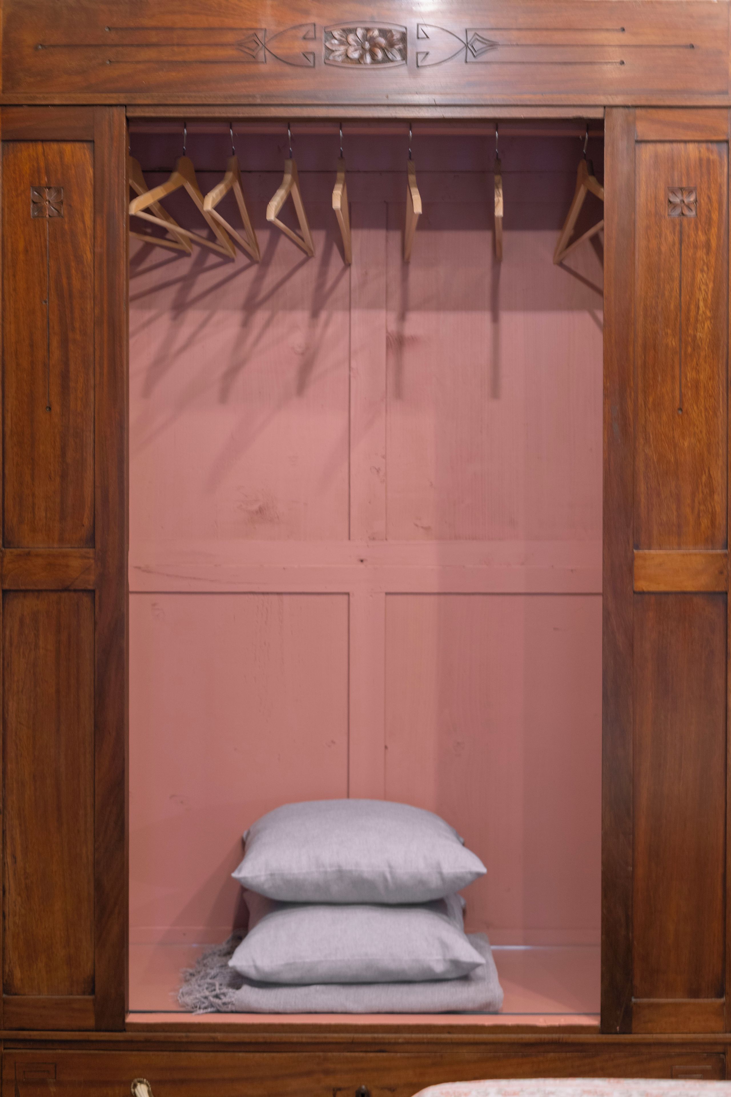 A wooden wardrobe with a pink interior, two hanging rods, and a single shelf at the bottom.