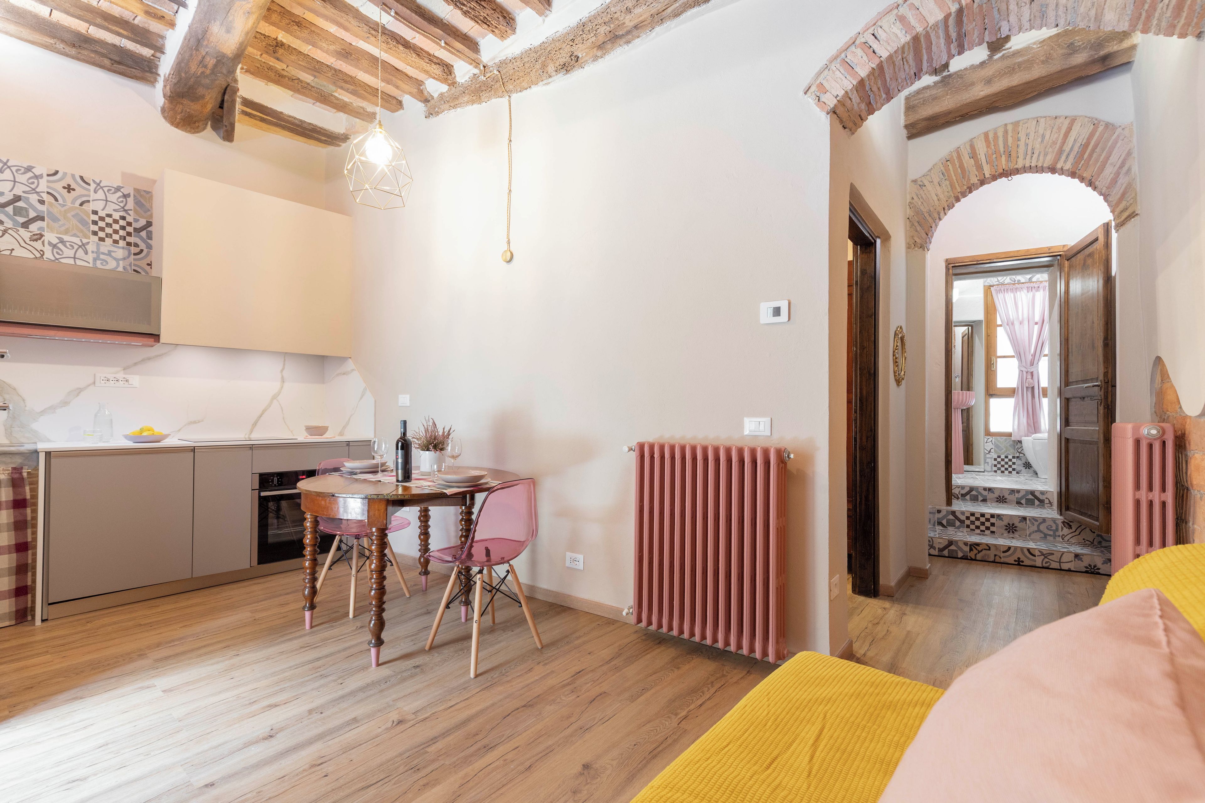A cozy kitchen with wooden beams, a dining table with chairs, and a view into a bathroom with a tiled floor.