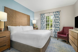 Hotelkamer met een groot bed, een houten hoofdeinde, een rode fauteuil, een televisie en een raam met gordijnen met een patroon.