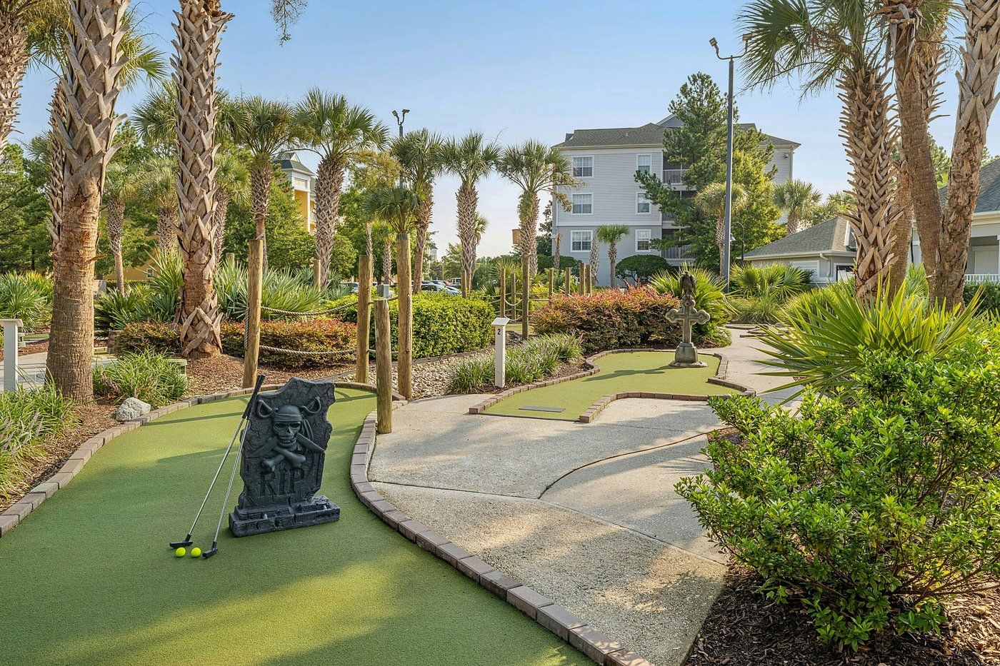 A miniature golf course with a pirate-themed hole, surrounded by palm trees and a building in the background.