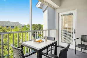 Een balkon met rieten meubilair, een tafel met een schaal oranje en een kopje, en een deur met zonwering.