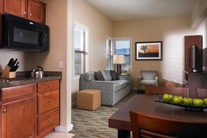 A compact living space with a kitchenette, a sofa, a dining table with apples, and a television. - Palm Desert | Friends Desert Retreat | Pool + Hot Tub | 2BR (Palm Desert)