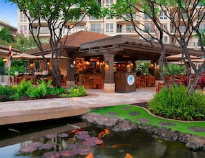 Ein Essbereich im Freien mit einer überdachten Terrasse, einem Teich mit Koikarpfen und einem Restaurant mit Außenplätzen.