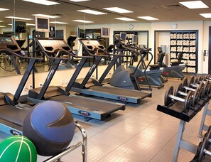 Une salle de sport équipée de plusieurs tapis de course, de bancs de musculation et de ballons d’exercice.