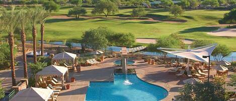 A pool area with lounge chairs and umbrellas, surrounded by a golf course and desert landscape.