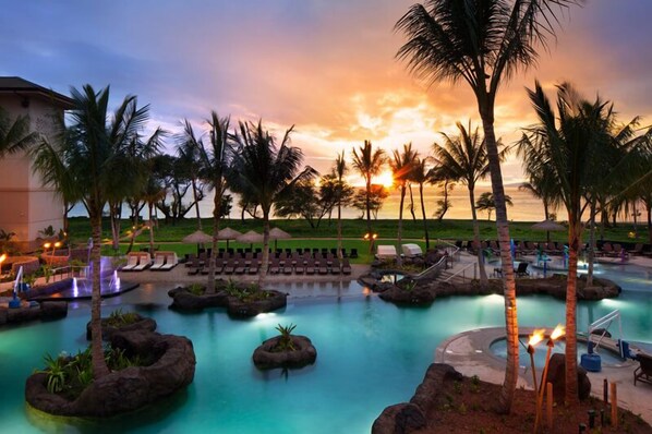 A resort pool area with multiple water features, palm trees, and lounge chairs. - Maui | Couples Island Weekend | Pool + Beach (Lahaina)