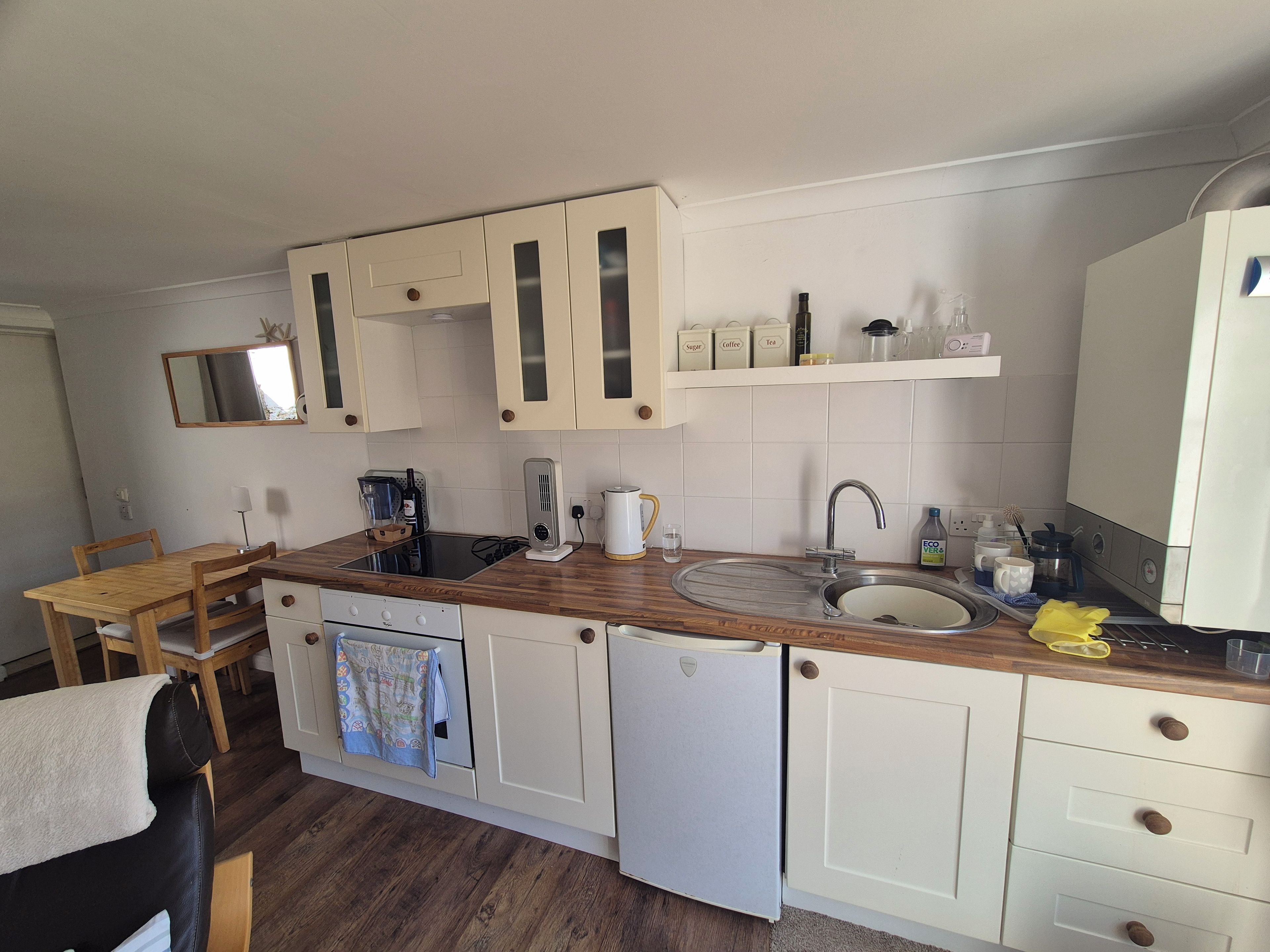 Een compacte keuken met witte kasten, een houten aanrecht, een spoelbak, een fornuis en een klein eethoekje met een tafel en stoelen.