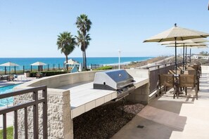 Zona de piscina amb una barbacoa, mobiliari exterior i ombrelles.