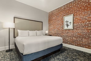 Una habitación de hotel con una cama, una mesita de noche, una lámpara, un muro de ladrillo y un cuadro enmarcado.