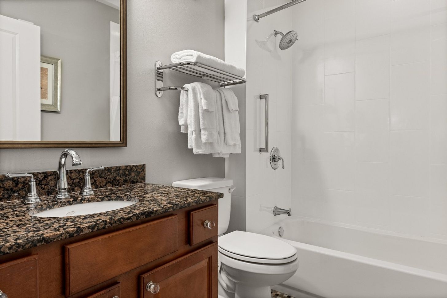 A bathroom with a granite countertop sink, a toilet, a shower, and a towel rack.