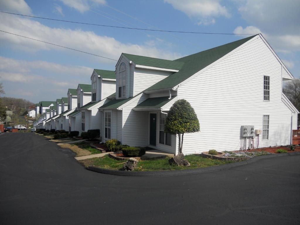 A row of white single-story houses with green roofs, arranged in a straight line along a street.