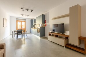 Una cocina moderna con armarios grises, un comedor con mesa y sillas, y un televisor de pantalla plana sobre un atril de madera.