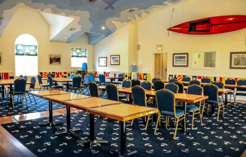A classroom with rows of tables and chairs, nautical-themed carpet, and a red lifeboat on the ceiling.