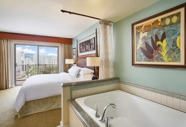 Une chambre d’hôtel avec un grand lit, une salle de bain avec baignoire et une vue sur la ville par la fenêtre.
