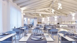 A modern restaurant with high ceilings, pendant lighting, and neatly arranged tables with blue chairs. - Piccolo Hotel (Porto Ottiolu)