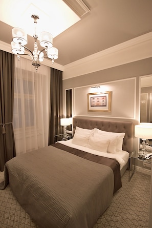 A hotel room with a large bed, a chandelier, a framed picture on the wall, and a bedside table with a lamp. - Hotel Jech (Hlavní město Praha)