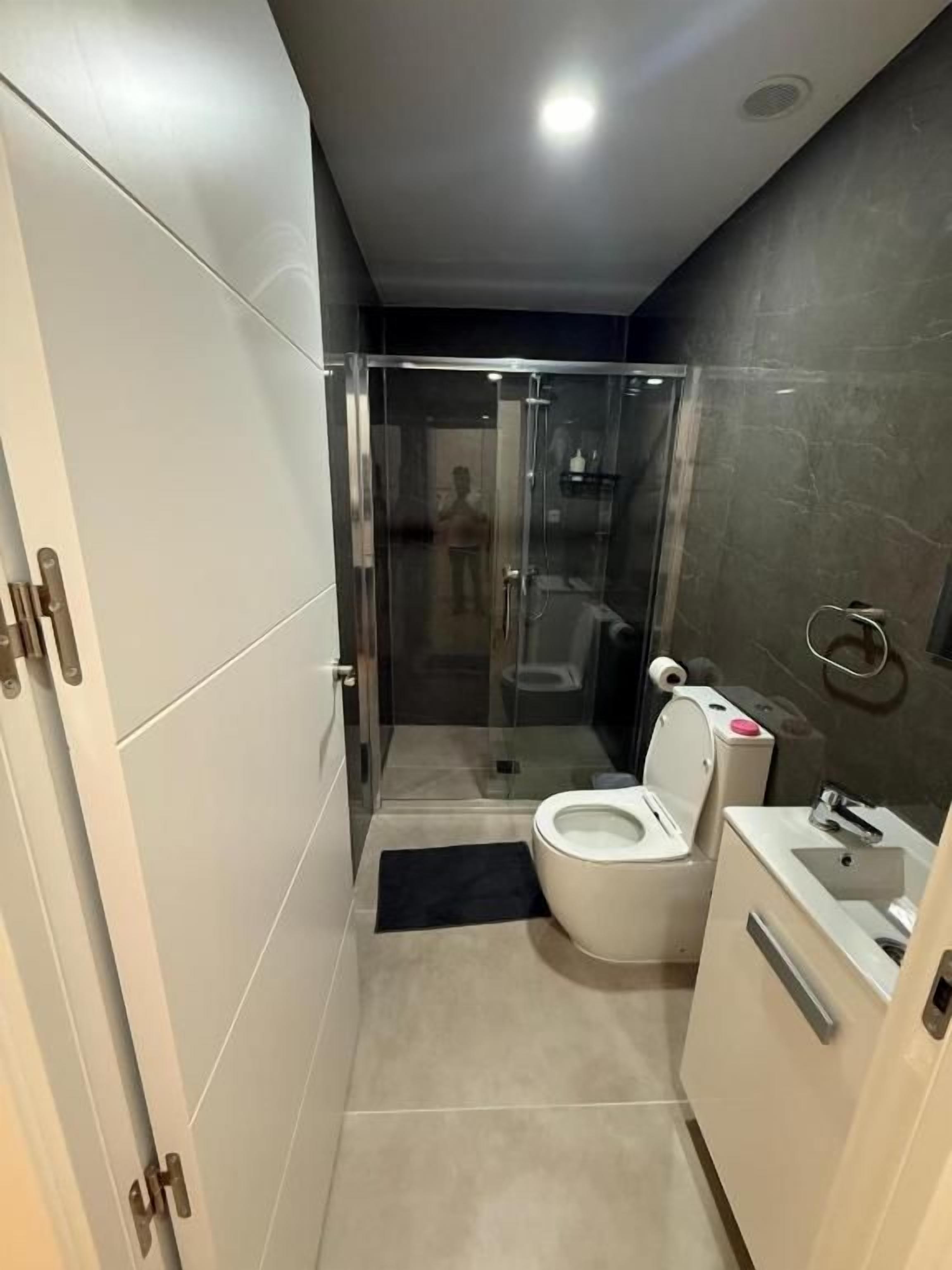 A modern bathroom with a glass-enclosed shower, a toilet, and a sink.