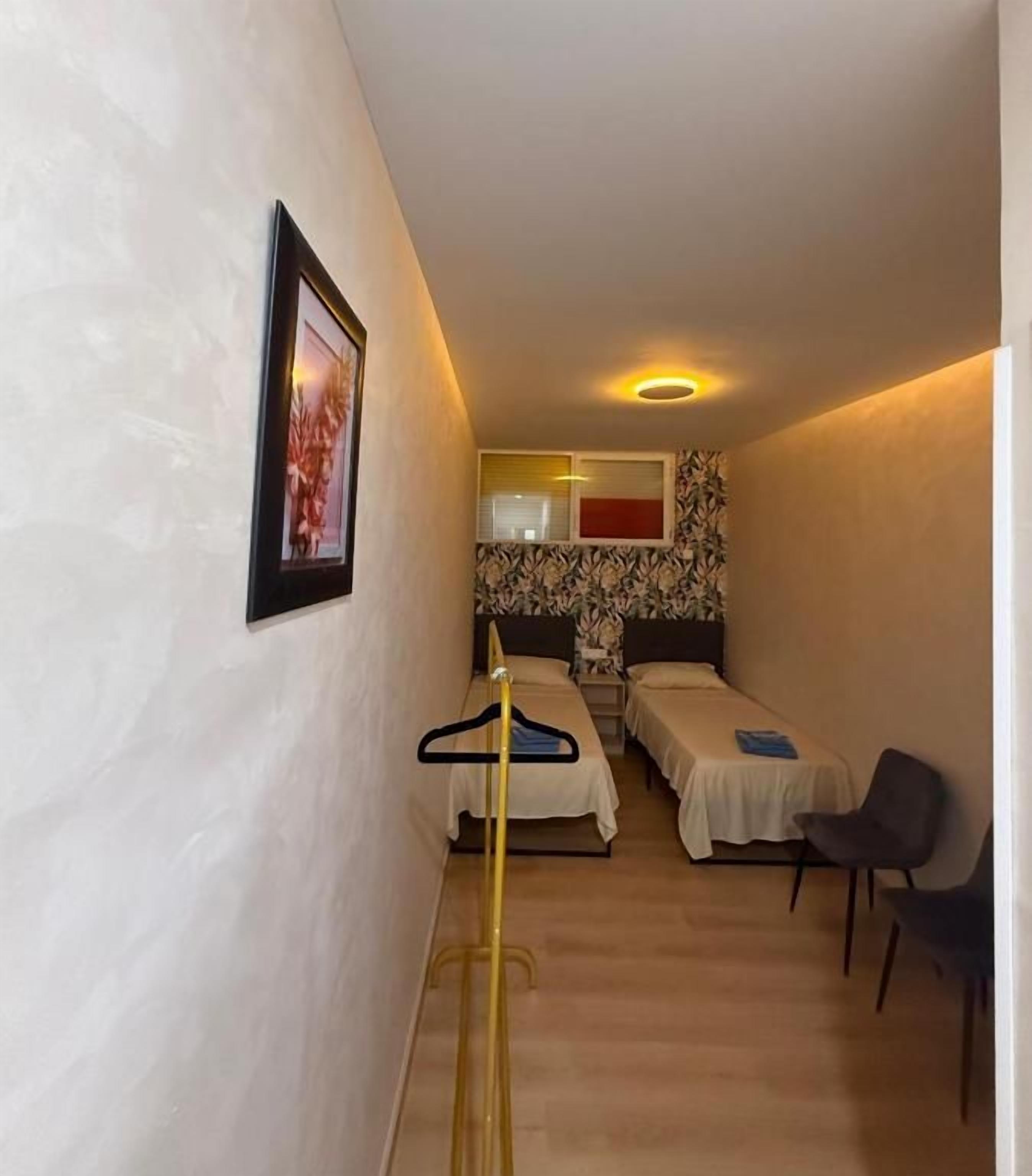 Une petite chambre d’hôtel avec un lit, une chaise, un bureau et un tableau accroché au mur.